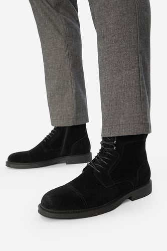 Model w d?ugich spodniach prezentuj?cy sznurowane buty za kostk?, uj?cie z do?u.