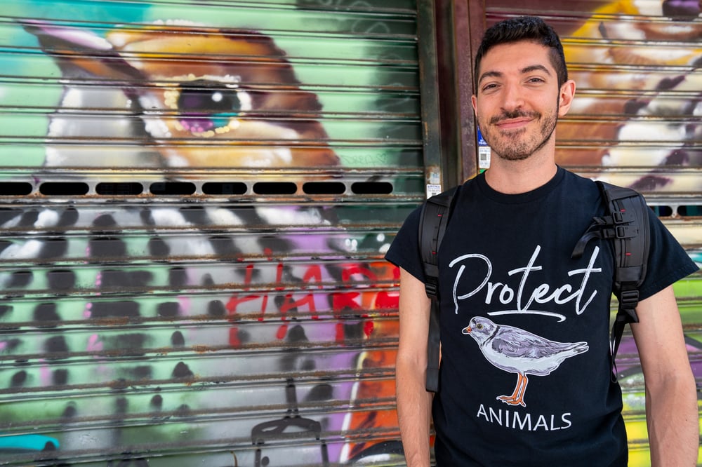Rocky Trifari beside a colorful bird mural, wearing a Protect Animals shirt