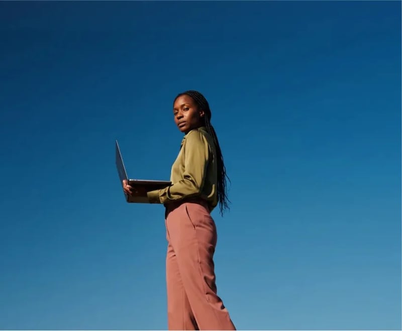 Woman holding an open laptop against a deep blue sky