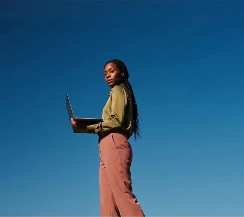Woman holding an open laptop against a deep blue sky