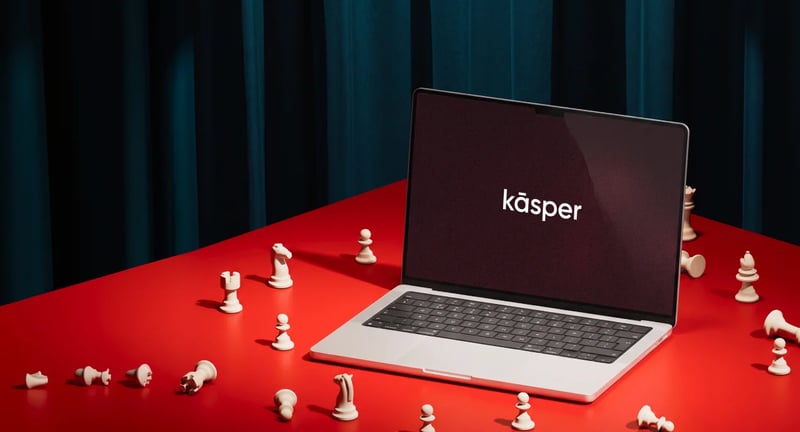 Laptop showing the Kāsper logo surrounded by chess pieces on a red table