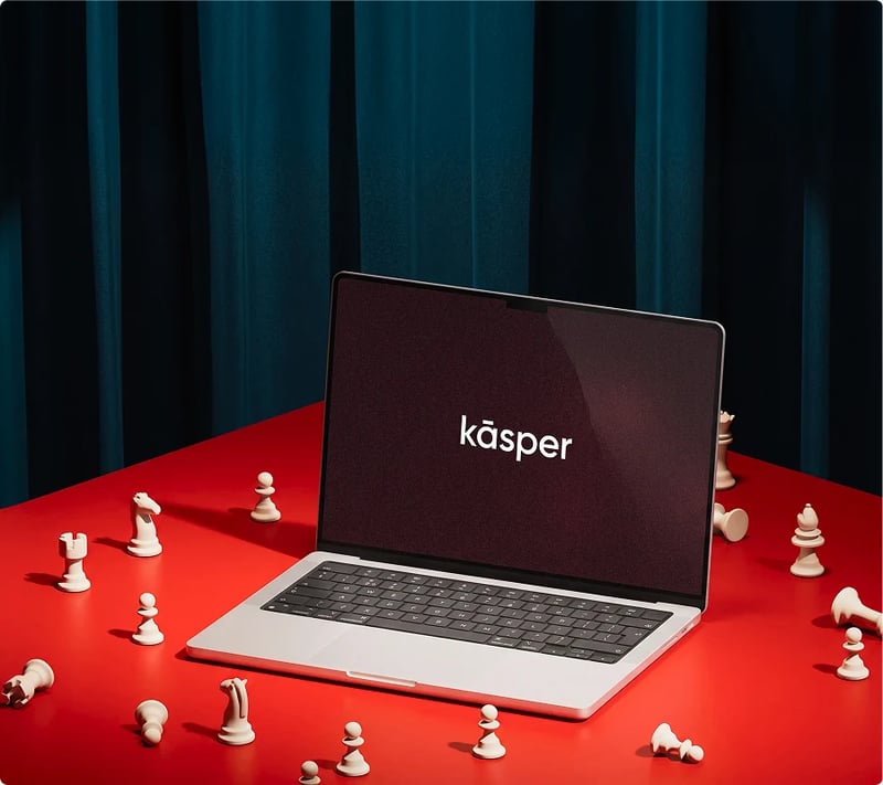 Laptop showing the Kāsper logo surrounded by chess pieces on a red table