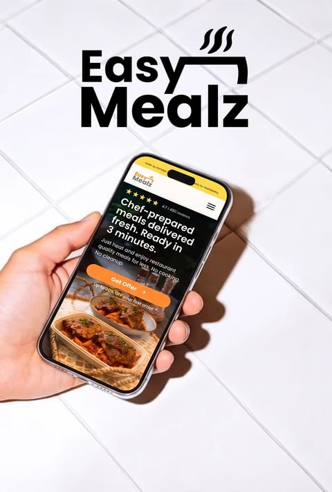 Easy Mealz meal delivery landing page on a phone held over white tiles