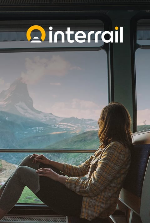 Interrail traveler looking out of a train window at snowy mountains