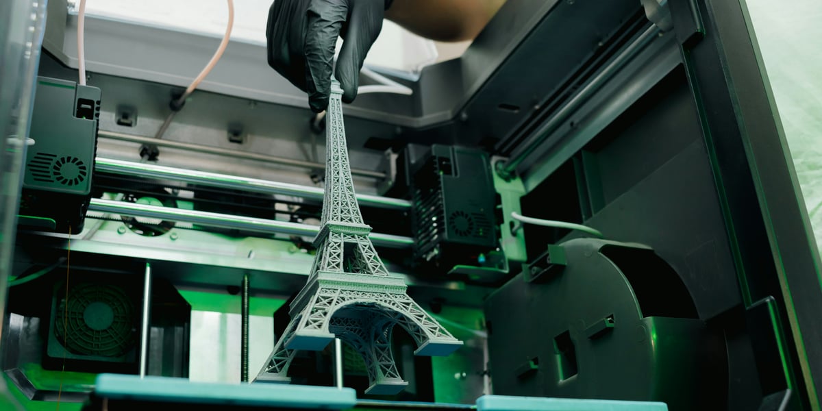 Detailní 3D model Eiffelovy věže vytištěný na profesionální 3D tiskárně v ochranné rukavici.