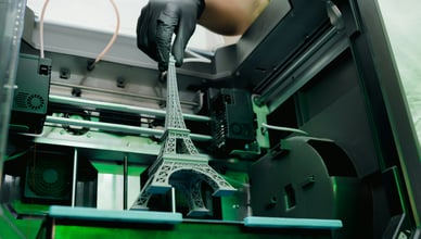 Detailní 3D model Eiffelovy věže vytištěný na profesionální 3D tiskárně v ochranné rukavici.