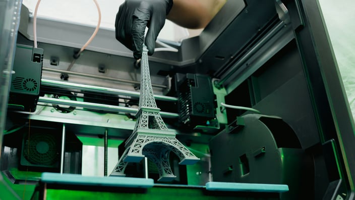 Detailní 3D model Eiffelovy věže vytištěný na profesionální 3D tiskárně v ochranné rukavici.