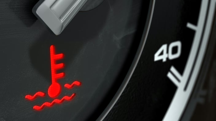 Detail palubní desky automobilu, kde svítí červená varovná kontrolka teploty chladicí kapaliny, což signalizuje přehřívání motoru.