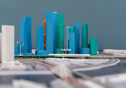 Detailní pohled na 3D vytištěný architektonický model města, který obsahuje vysoké budovy v modré a zelené barvě a silniční infrastrukturu. Model s nápisem "Praha" ilustruje, jak se 3D tisk používá pro detailní a realistické architektonické vizualizace.