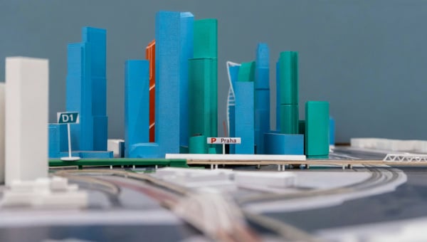Detailní pohled na 3D vytištěný architektonický model města, který obsahuje vysoké budovy v modré a zelené barvě a silniční infrastrukturu. Model s nápisem "Praha" ilustruje, jak se 3D tisk používá pro detailní a realistické architektonické vizualizace.