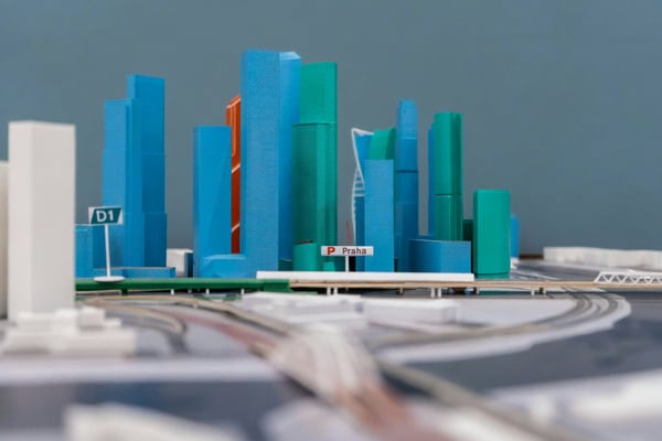 Detailní pohled na 3D vytištěný architektonický model města, který obsahuje vysoké budovy v modré a zelené barvě a silniční infrastrukturu. Model s nápisem "Praha" ilustruje, jak se 3D tisk používá pro detailní a realistické architektonické vizualizace.
