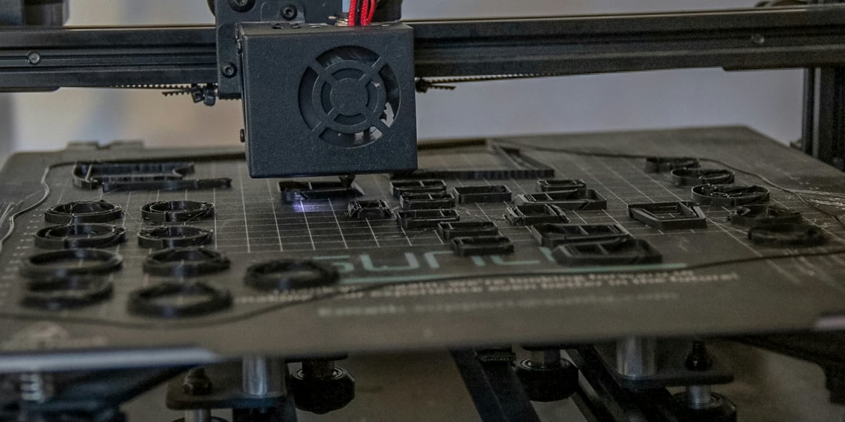 Ruce v rukavicích brousí 3D tištěný model, v pozadí jsou vidět nástroje pro post-processing jako štětce, barvy a tmely. Ilustruje proces dokončovacích prací na 3D výtisku.