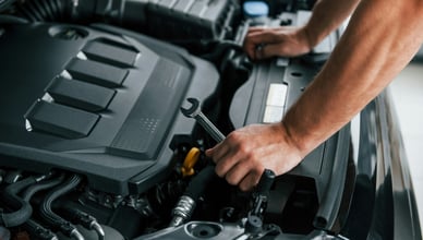 Крупный план рук механика с ключом, выполняющего техническое обслуживание двигателя и замену свечей зажигания.