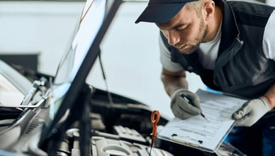 Automechanik provádí předprodejní kontrolu vozu na zvedáku a zapisuje technický stav do protokolu o stavu vozidla.