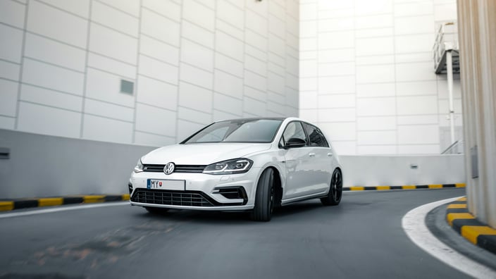 Volkswagen Golf R Mk7 facelift v pohybu na rampě moderního parkovacího domu s černými koly a panoramatickou střechou.