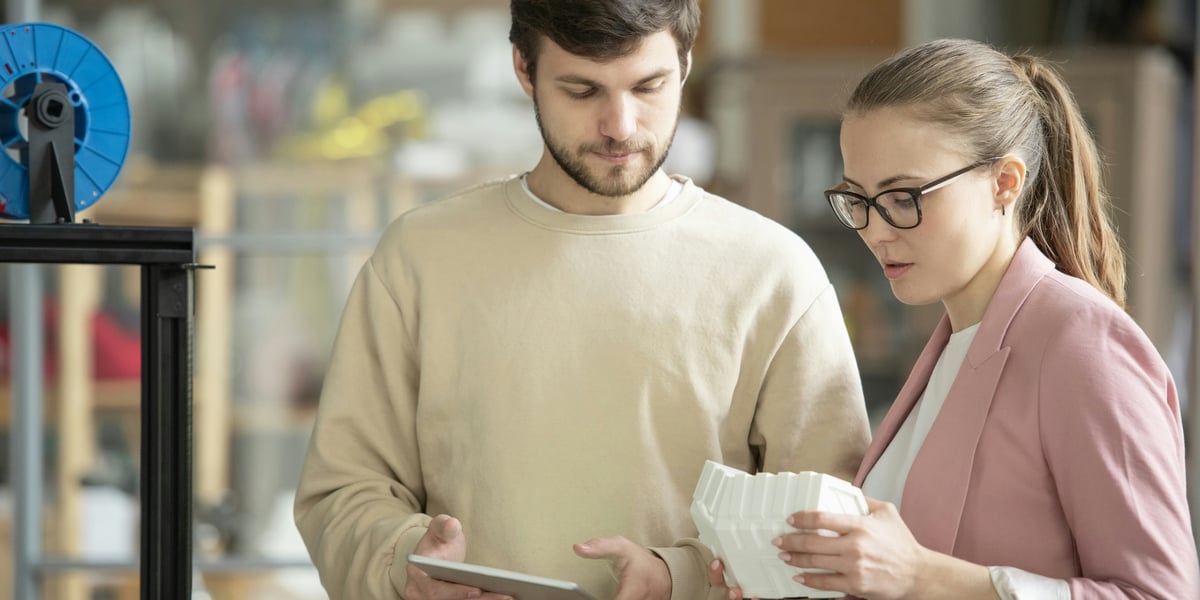 Studenti a učitelé se učí pracovat s 3D tiskárnou ve třídě, s notebookem zobrazujícím 3D model krychle v popředí, symbolizující STEM vzdělávání.