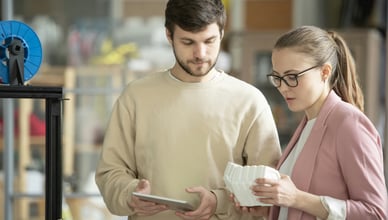 Studenti a učitelé se učí pracovat s 3D tiskárnou ve třídě, s notebookem zobrazujícím 3D model krychle v popředí, symbolizující STEM vzdělávání.