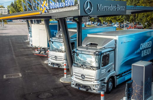 Elektrické nákladní vozy Mercedes-Benz eActros u nabíjecí stanice, demonstrující naši odbornost v údržbě komerčních flotil elektromobilů.