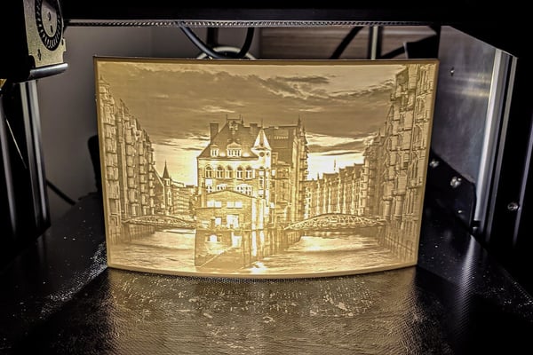 3D tiskárna vytváří světle zbarvený, průsvitný obraz města s řekou a budovami. Objekt je typickým příkladem litofánie, což je 3D vytištěná fotografie, která září při osvětlení a je ideálním personalizovaným dárkem.