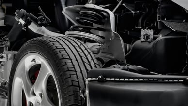 Detail odhaleného systému zavěšení předního kola automobilu, který ukazuje kolo, pneumatiku, brzdový třmen a komplexní součásti sestavy tlumiče a pružiny. Tento obrázek názorně vysvětluje klíčové části podvozku a zdůrazňuje význam dobře udržovaných tlumičů pro bezpečnost, ovladatelnost a jízdní komfort. Perfektní pro články o funkci tlumičů, známkách opotřebení a profesionálních opravách zavěšení kol.