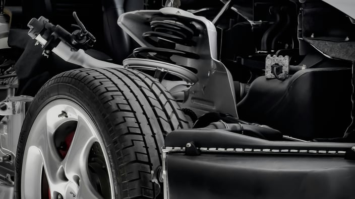 Detail odhaleného systému zavěšení předního kola automobilu, který ukazuje kolo, pneumatiku, brzdový třmen a komplexní součásti sestavy tlumiče a pružiny. Tento obrázek názorně vysvětluje klíčové části podvozku a zdůrazňuje význam dobře udržovaných tlumičů pro bezpečnost, ovladatelnost a jízdní komfort. Perfektní pro články o funkci tlumičů, známkách opotřebení a profesionálních opravách zavěšení kol.