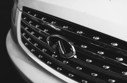 Логотип Infiniti на хромированной решётке радиатора роскошного автомобиля, символизирующий наши специализированные услуги по ремонту для премиальных брендов.