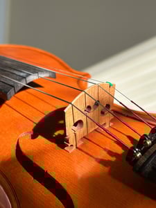 Detailní pohled na dřevěné housle, zaměřený na kobylku a struny. Obrázek ilustruje preciznost a detail, které jsou klíčové pro 3D tisk hudebních nástrojů a jejich částí.