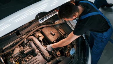 Механик с фонариком проверяет двигатель автомобиля, сосредоточен на генераторе и стартере для диагностики проблем с электросистемой.