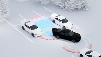 Černé auto couvá z parkovacího místa a jeho senzorové systémy jsou znázorněny červeným a modrým světlem, které detekují bílé auto vpravo.