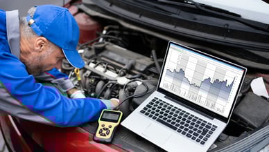 Automechanik provádí diagnostiku motoru vozu pomocí notebooku a diagnostického nástroje, aby odhalil a předešel potenciálním drahým opravám.