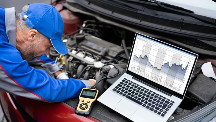 Automechanik provádí diagnostiku motoru vozu pomocí notebooku a diagnostického nástroje, aby odhalil a předešel potenciálním drahým opravám.