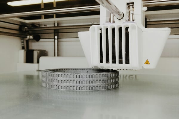 3D tiskárna vytváří detailní model v šedé barvě, který připomíná oblouky starověkého Kolosea. Ilustrace použití 3D tisku pro obnovu historických památek a artefaktů.