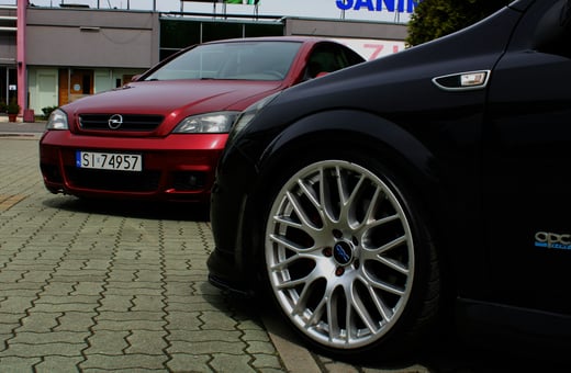 Колесо мощного хэтчбека Opel Astra OPC на фоне второго красного Opel, что показывает наше внимание к производительности и точности ремонта.
