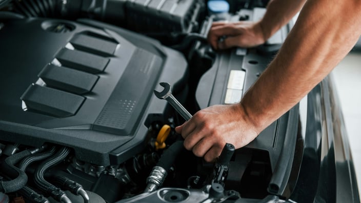Automechanik provádí kontrolu a údržbu motoru v autoservisu, v ruce drží klíč připravený k odborné opravě.