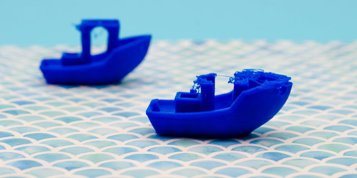 Dvě modré 3D tištěné lodičky na vzorovaném podkladu jako ukázka prvního úspěšného tisku