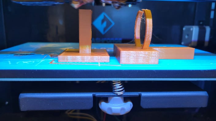 Detailní záběr na 3D tištěný plastový díl, který nahrazuje originální rozbitou součástku, ležící vedle šroubováku a dalších nástrojů.