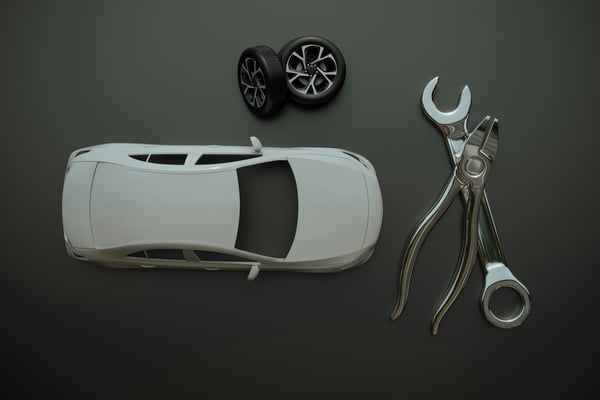 Přehledný pohled shora na 3D model bílého automobilu s dvojicí kol a velkým klíčem s kleštěmi na tmavě šedém pozadí. Předměty ilustrují zakázkovou výrobu automobilových dílů a prototypů pomocí 3D tisku.