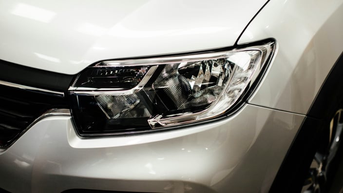 Detailní záběr na čistý a vyleštěný přední světlomet bílého moderního automobilu.