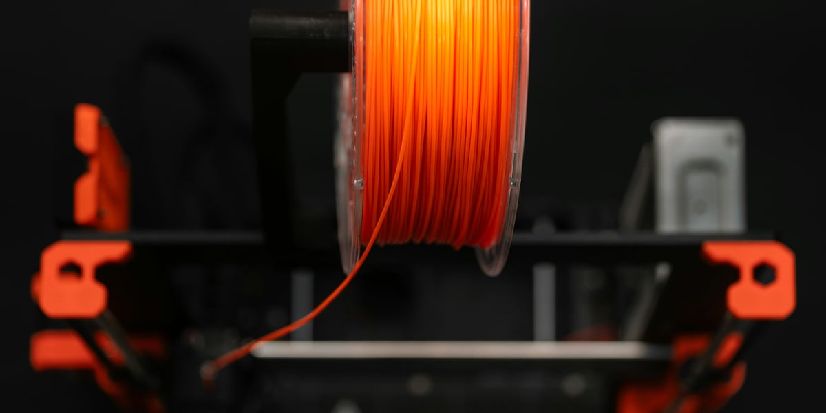 Oranžový 3D tiskový filament navinutý na cívce, připravený k použití v 3D tiskárně, se zaostřením na samotný materiál.