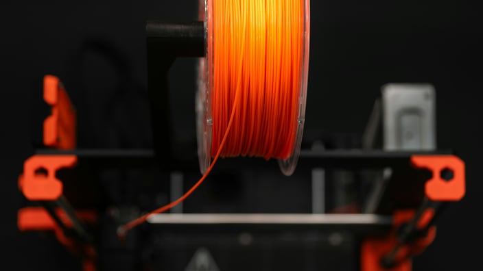 Oranžový 3D tiskový filament navinutý na cívce, připravený k použití v 3D tiskárně, se zaostřením na samotný materiál.