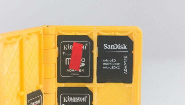 Otevřené žluté 3D vytištěné pouzdro, ve kterém jsou uložené paměťové karty microSD. Pouzdro je příkladem personalizovaného doplňku pro elektronické gadgety, který je možné vytvořit na míru.