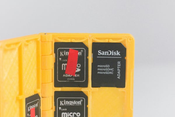 Otevřené žluté 3D vytištěné pouzdro, ve kterém jsou uložené paměťové karty microSD. Pouzdro je příkladem personalizovaného doplňku pro elektronické gadgety, který je možné vytvořit na míru.