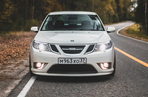 Классический белый седан Saab 9-3 на живописной дороге, указывающий на наш специализированный сервис для взыскательных автовладельцев и уникальных брендов.