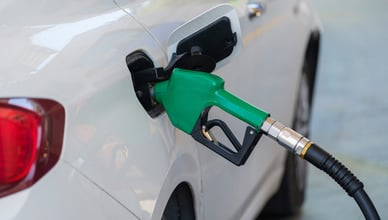 Zelená tankovací pistole zasunutá v nádrži bílého osobního automobilu na čerpací stanici.