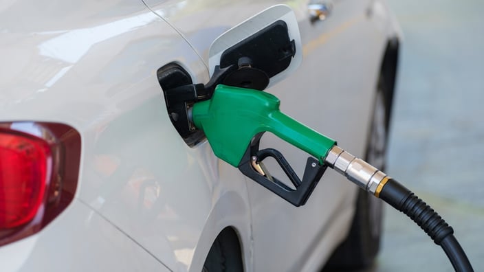Zelená tankovací pistole zasunutá v nádrži bílého osobního automobilu na čerpací stanici.