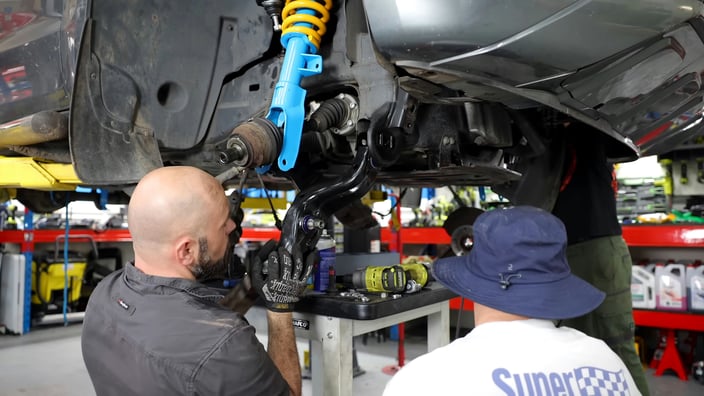 Automechanik v profesionálním autoservisu provádí opravu podvozku a montuje nové díly zavěšení, jako je tlumič a rameno nápravy, na voze zvednutém na zvedáku.