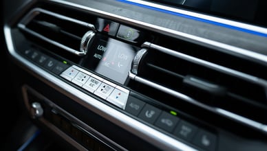 Detailní pohled na moderní ovládací panel klimatizace v autě s digitálním displejem a výdechy ventilace.