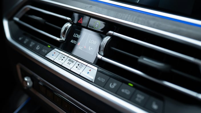 Detailní pohled na moderní ovládací panel klimatizace v autě s digitálním displejem a výdechy ventilace.