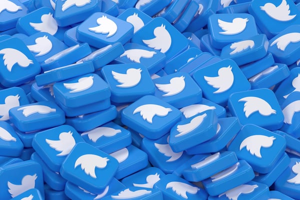 Hromada modrých 3D vytištěných reklamních produktů ve tvaru ikon s bílým logem ptáka uprostřed. Ilustruje možnosti 3D tisku pro výrobu velkého množství personalizovaných propagačních předmětů pro firmy.