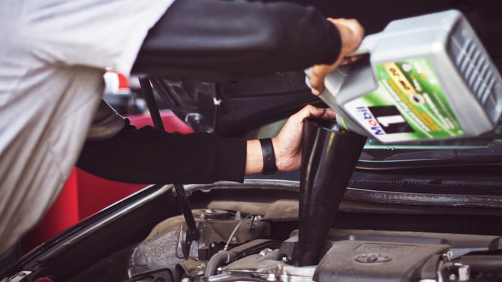 Automechanik provádí profesionální výměnu oleje a doplňuje nový motorový olej do motoru vozidla v autoservisu.